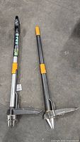 Two long-handle weed removal tools side by side, showing ergonomic handles and metal construction with forked and digging blades.