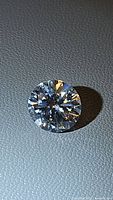 Close-up photo of a loose round brilliant cut 3.55ct moissanite stone on a textured surface, showing facets and brilliance