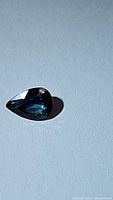 Photo of pear cut natural blue sapphire on a light background showing blue reflective facets and clarity.