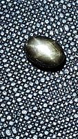 Oval untreated black star sapphire on a textured black surface showing the golden 6-ray star effect reflecting light.