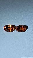 Pair of oval cut natural imperial sapphires laying side by side on a neutral surface, showing their bright fire orange color and facets.