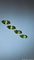 Four natural marquis cut apple green peridot gemstones arranged horizontally.