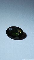Oval cut natural green sapphire displayed under light showing facets and forest green color.