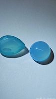 Two natural blue chalcedony gemstones, one faceted pear-shaped and one smooth round cabochon, displayed on a white background under natural light to show color and translucency.