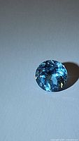 High resolution photo showing the round cut, clear facets, and sky blue color of the natural blue topaz gemstone under lighting.