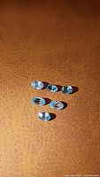 Six natural blue zircon oval cut gemstones arranged in two rows on a brown surface, showing clarity and blue color.