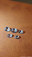 Five natural Brazilian aquamarine gemstones with mixed cuts arranged on a brown surface, showing clarity and light blue color.