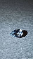 Close-up photo of a natural pear cut aquamarine gemstone, showing faceting and light blue color.