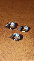 Three pear-shaped natural aquamarine gemstones placed on a brown surface, showing facets and light reflections.