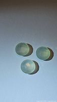 Three smooth, oval cabochon chalcedony stones with a pale green tea coloring, photographed on white surface under light showing their translucency.