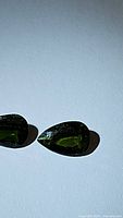 Pair of pear shaped vivid green natural Russian chrome diopside gemstones with visible internal inclusions under bright light on a plain background.