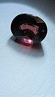 Close-up image of a natural oval cut pink-purple tourmaline gemstone with visible multicolored flashes and deep color saturation.