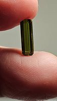 Close-up of bright green, octagon cut tourmaline gemstone held between fingers showing elongated shape and facet detail.