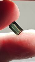 Natural untreated green tourmaline gemstone, octagon cut shown held between fingers in natural light to display color and cut.