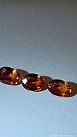 Three oval natural imperial sapphires with rich orange hues on a flat surface under direct light showing facets and color.