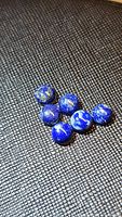 Six polished round lapis lazuli cabochons with natural inclusions on black textured surface