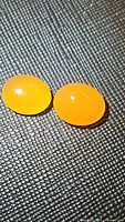 Two natural mandarin orange carnelian oval cabochon gemstones shown on a textured black surface with front lighting highlighting their smooth surface and rich color.