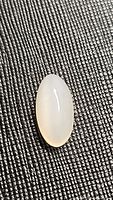 Single oval marquis white cats eye moonstone cabochon on a textured black background showing color and chatoyancy.