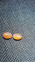 Pair of natural peach-colored oval moonstone cabochons with oval smooth polished surfaces, showing faint cat's eye effect, on a textured dark background.