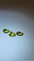 Three natural apple green peridot gemstones displayed on a white surface showing their pear and oval cuts and bright clarity.