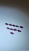 Photo of 10 marquis cut rubies arranged in two curved lines on a white surface showing deep pink red natural untreated gemstones.