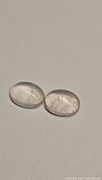 Close-up photo of two natural oval rose quartz cabochons with a smooth polished finish.