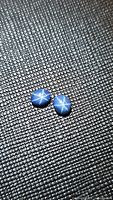 Two natural blue star sapphire cabochons showing a bright six-ray star effect on textured dark surface.