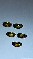Photo showing five oval cut natural tourmaline gemstones in various yellow, green, and orange tones laid on a flat surface.