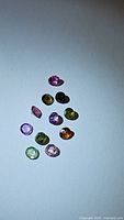 Single photo showing 11 round cut multicolor natural tourmaline gemstones arranged on a flat surface.