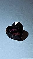 Heart-cut deep pink tourmaline gemstone photographed on a flat surface showing facets and color under light.