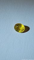 Oval natural canary yellow sapphire gemstone against a light background, showing vivid color and faceting from the top view.
