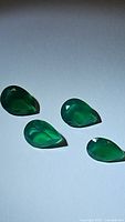 Four pear-shaped green onyx stones arranged on flat surface under direct light, showing color and translucency.