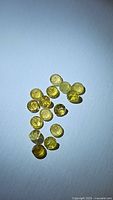 Top-down photo of multiple loose natural yellow round cut tourmaline gemstones arranged together on a white surface.