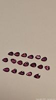 21 pear-cut untreated natural rubies laid out on a plain surface showing deep red to purplish-red color and clarity.