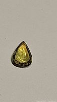 Close-up photo of a natural chartreuse pear cut sapphire gemstone on a plain background.