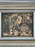 Close-up of framed woodcut showing theatrical scene and characters in period dress, black ink on paper.