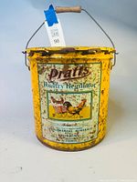 Front view of the antique yellow Pratts Poultry Regulator tin bucket showing lithographed graphics, text and wooden handle.