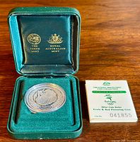 Front view of coin displayed in green case alongside certificate of authenticity.