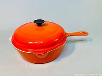 Orange enamelled cast iron cooking pot with lid, side angle showing handle and spout