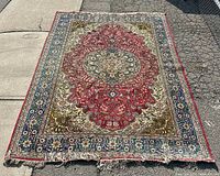 Full-length view of rectangular carpet laid on pavement, showing overall red field with central medallion and multicolored borders