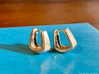 Pair of silver hoop earrings displayed on a blue box with clear view of their modern geometric shape and thickness.
