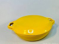 Yellow round covered cast iron pot with lid, showing overall exterior shape and color.