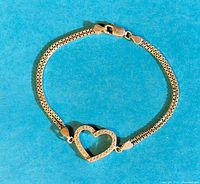 Sterling silver bracelet with open heart charm studded with cubic zirconia stones on a turquoise background