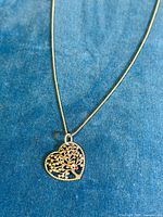 Close-up of the heart-shaped pendant with tree design and red stone on blue background showing details and finish.