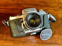 Front angled view of vintage Miranda G camera with attached Soligor lens and Miranda lens cap on wooden table.