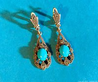 Pair of vintage turquoise and marcasite sterling silver dangle earrings on a blue background.