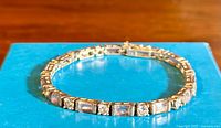 Photo of tennis bracelet laid flat on a blue box showing alternating rectangular amethyst and round clear stones set in silver.