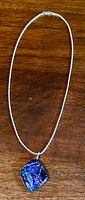 Full view of the necklace with the pendant on a wooden surface, showing the pendant's vibrant iridescent colors and sterling silver chain.