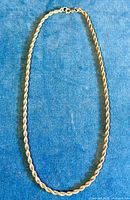 Full view of the twisted rope silver chain necklace laid flat on blue fabric background showing entire length and clasp.