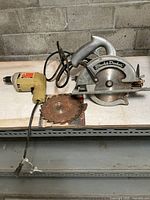 Black & Decker circular saw and corded drill with power cords, visible wear, and a spare circular saw blade.